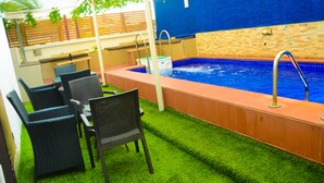 Uma área de piscina com grama sintética, uma banheira de hidromassagem e mobiliário de vime.