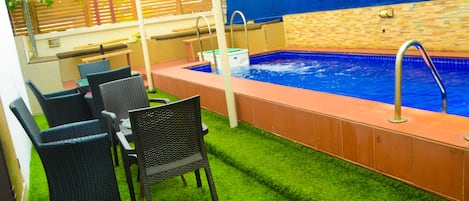 A pool area with artificial grass, a hot tub, and wicker furniture.