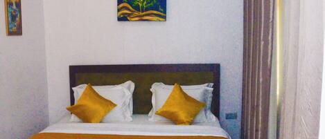 A hotel room with a bed, a bench, a painting, and an air conditioning unit.