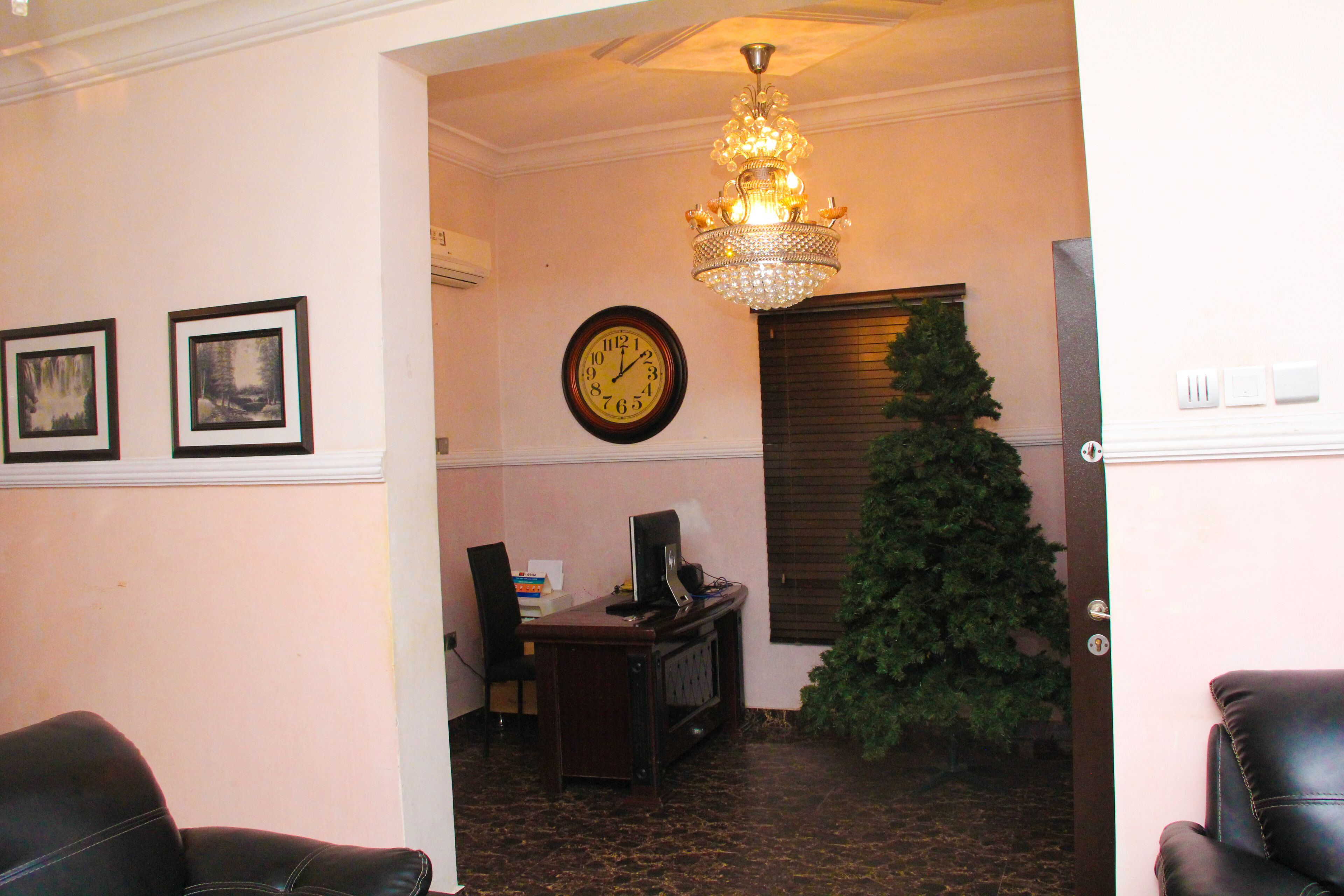 Une pièce comprenant un bureau, une chaise, une horloge, un sapin de Noël et un lustre.