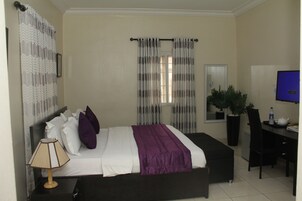 A hotel room with a bed, a desk, a chair, a television, and a potted plant.
