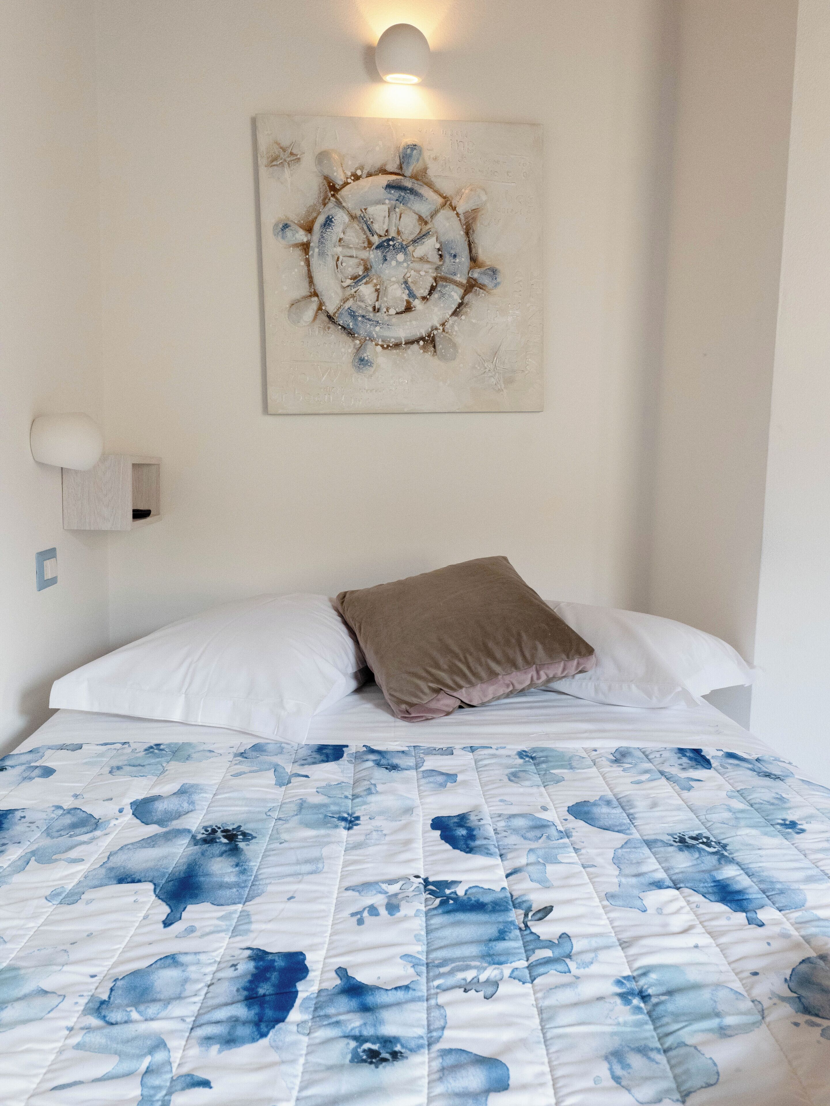 Un dormitorio con una cama, una lámpara fijada a la pared y un cuadro.
