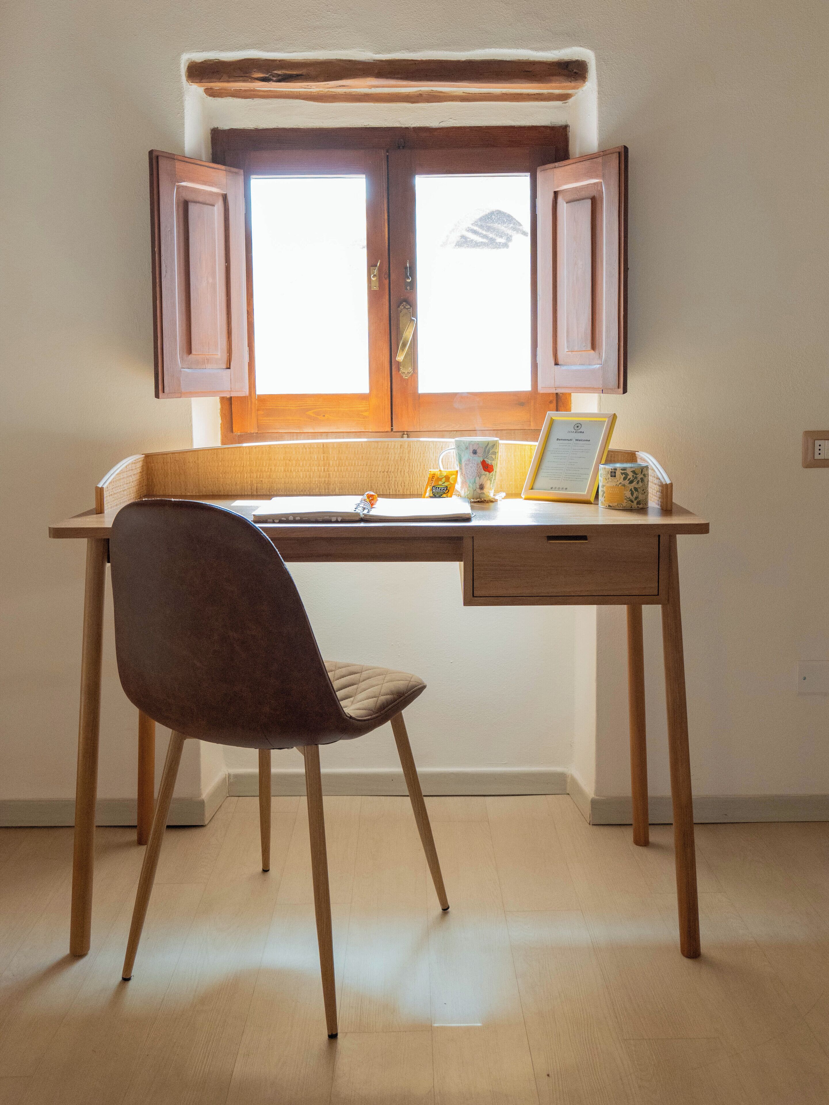 Ein Arbeitszimmer mit Schreibtisch, Stuhl und zwei Fenstern mit Holzrollläden.