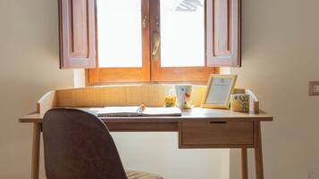 Ein Arbeitszimmer mit Schreibtisch, Stuhl und zwei Fenstern mit Holzrollläden.