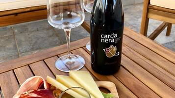 Una mesa de madera con una botella de vino, copas y una tabla de embutidos con carnes, queso, aceitunas y tomates.