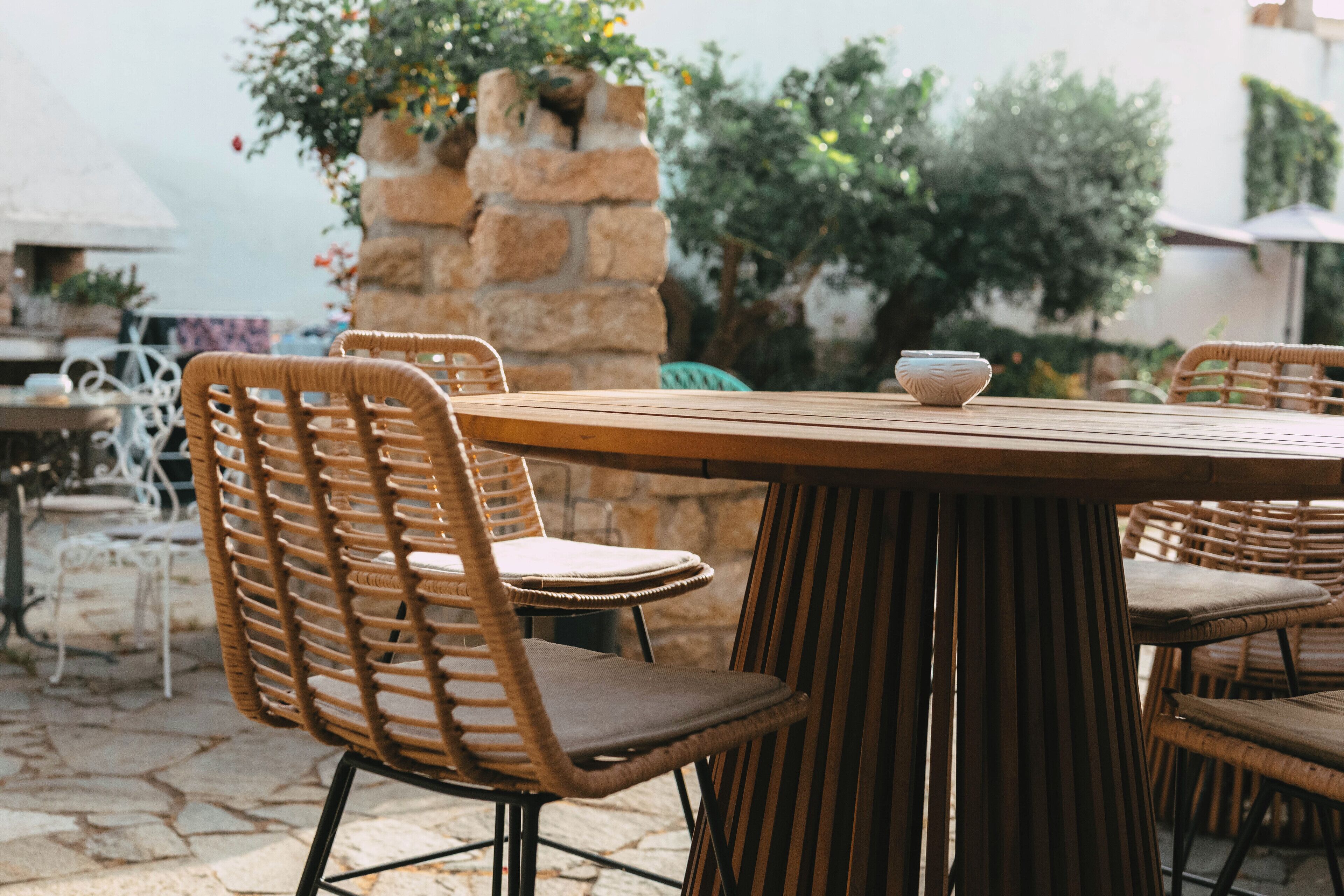 Una mesa redonda de madera con sillas de mimbre, una pared de piedra y follaje al fondo.