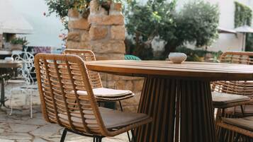 Una mesa redonda de madera con sillas de mimbre, una pared de piedra y follaje al fondo.