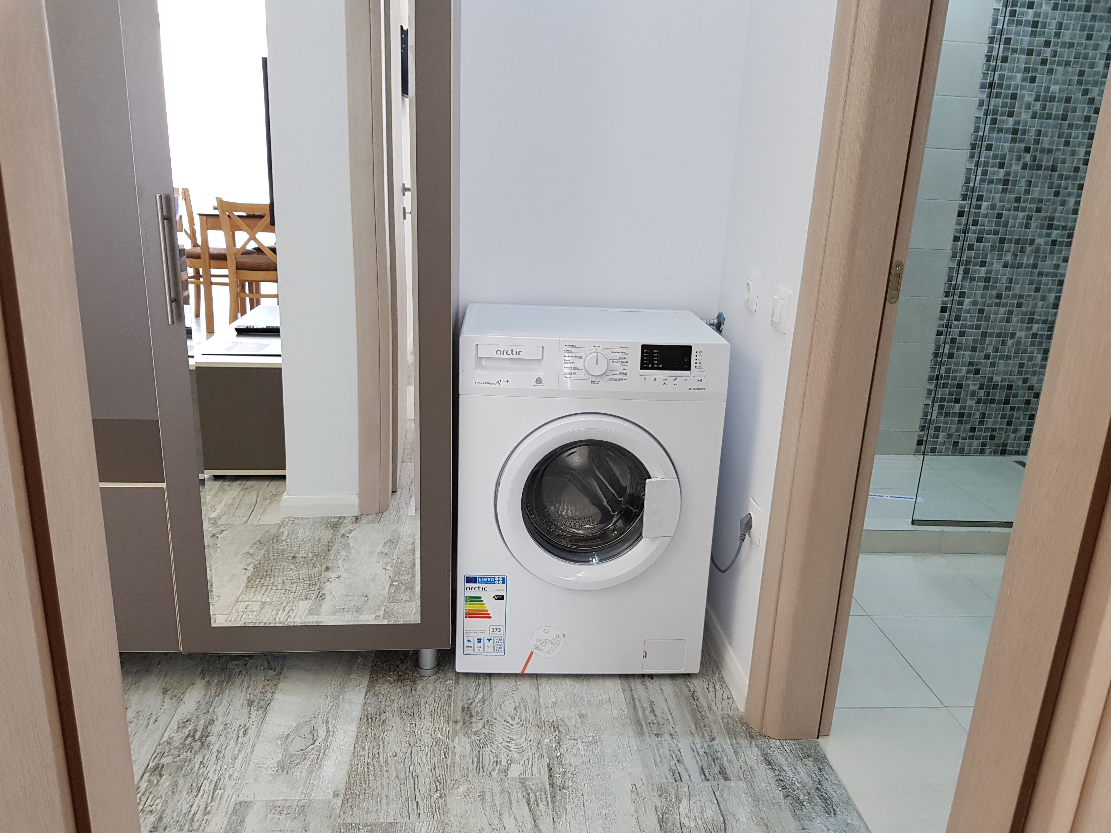 A compact laundry room with a front-loading washing machine, a tiled floor, and a glass shower area.