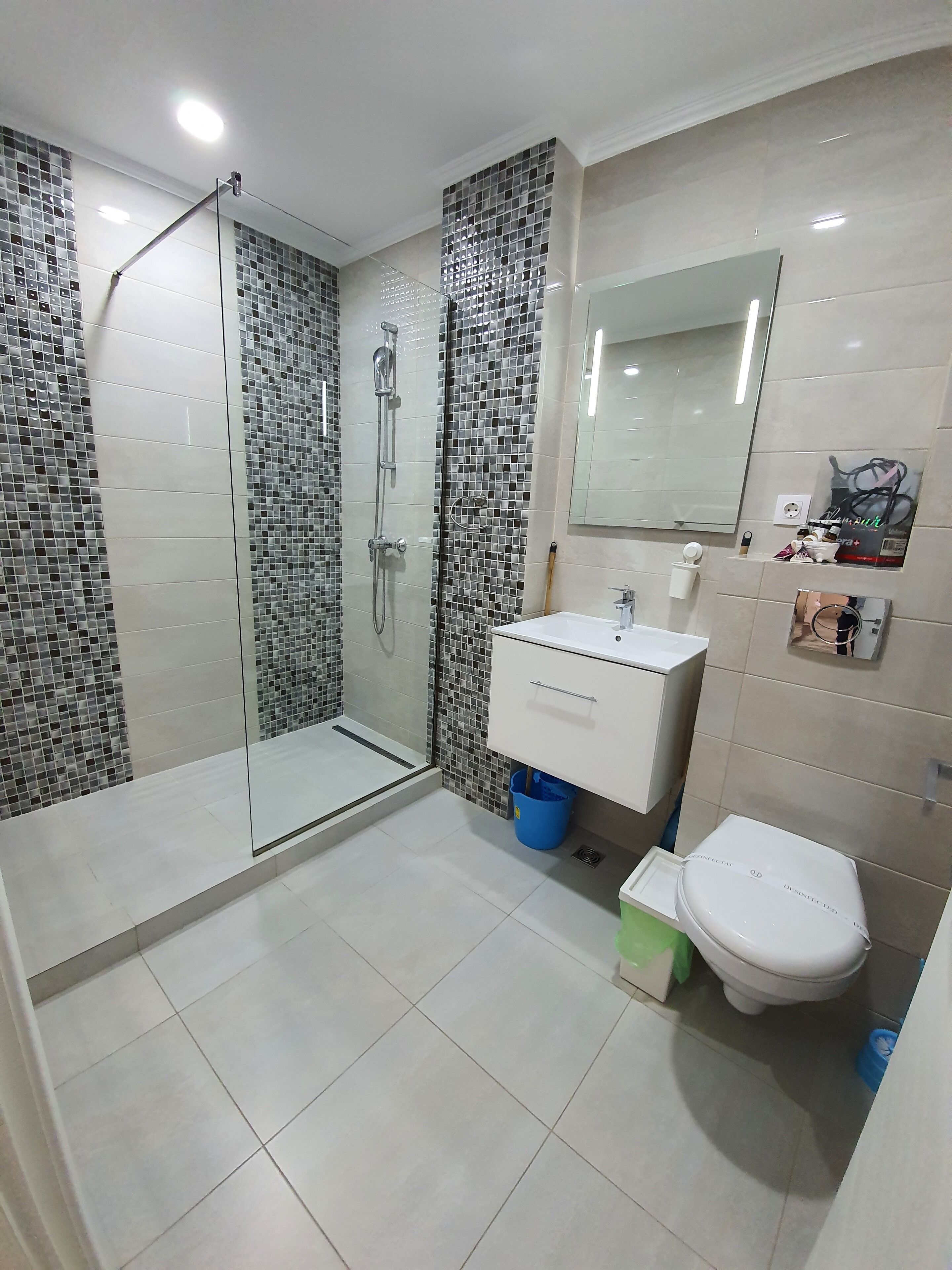 Un baño moderno con cabina de ducha de vidrio, azulejos blancos, un lavabo blanco y un inodoro.