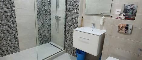 A modern bathroom with a glass shower enclosure, white tiles, a white sink, and a toilet.