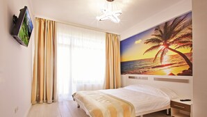 Een hotelkamer met een bed, een nachtkastje, een aan de muur bevestigde televisie en een schilderij van een zonsondergang boven de oceaan.