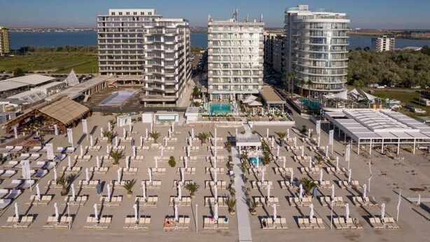 Een hotel met meerdere hoge gebouwen, een groot zwembad en een strand met ligbedden.