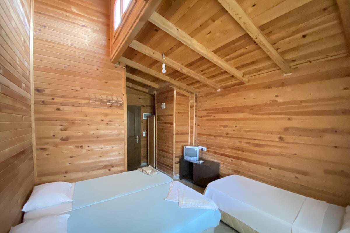Une chambre dans un chalet en bois, avec deux lits, un petit bureau équipé d’un ordinateur et une fenêtre.