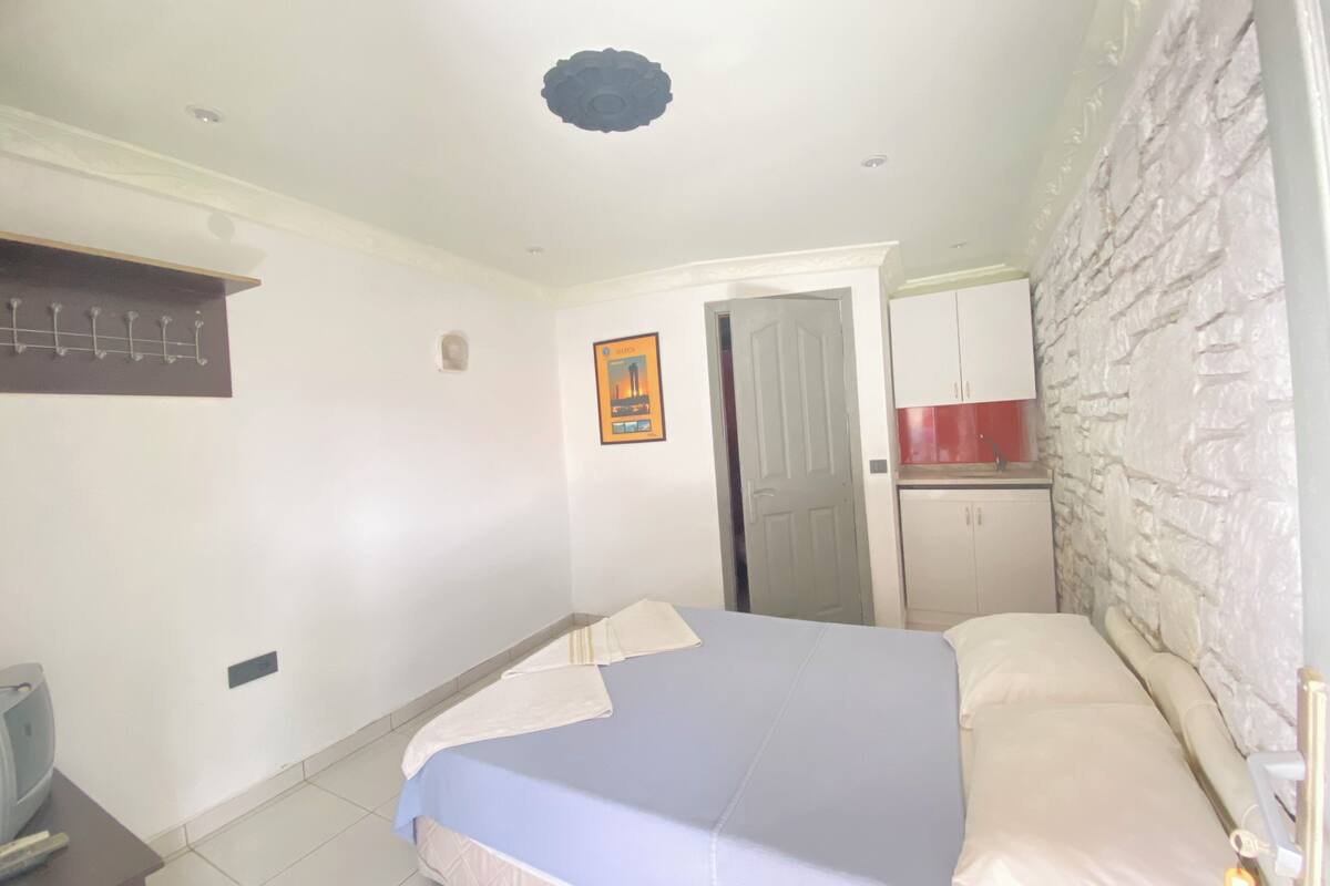 Une chambre comprenant un lit, une armoire, un petit coin cuisine et une porte donnant sur une autre pièce.