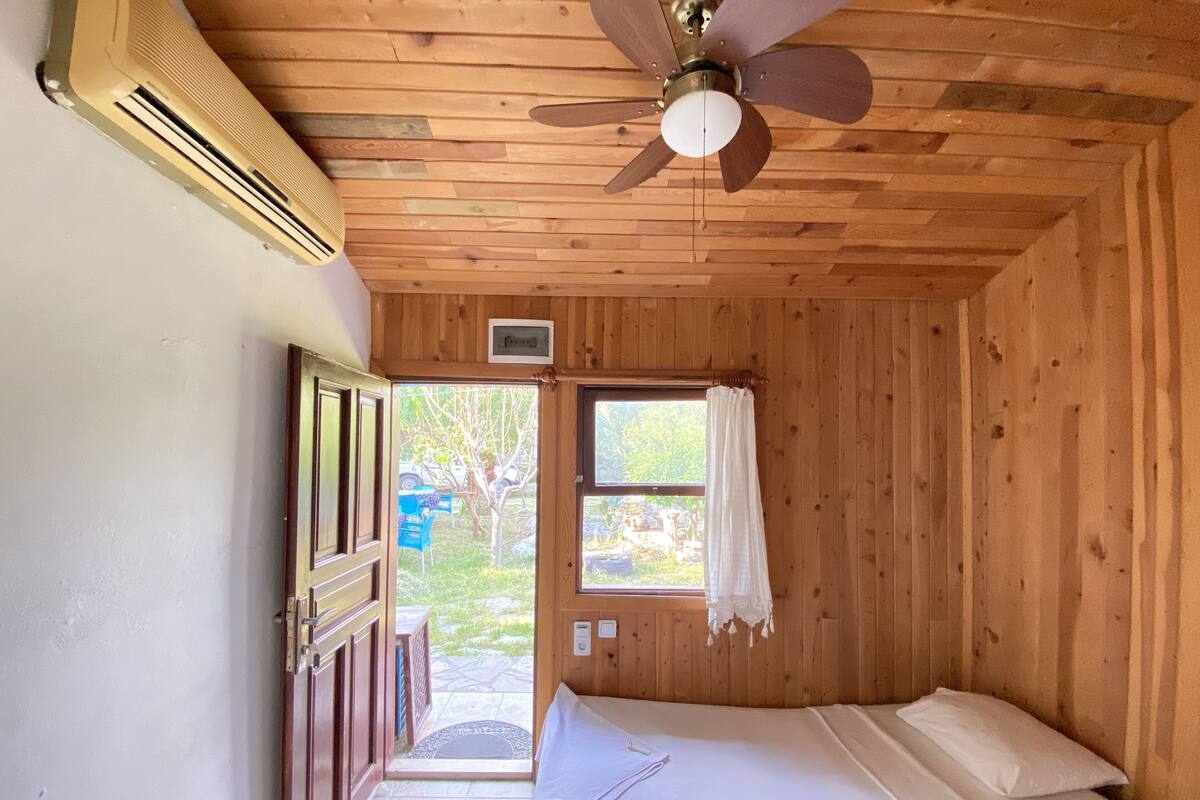 Une pièce en bois avec un lit, un ventilateur de plafond, une fenêtre avec des rideaux et un appareil de climatisation.