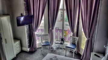 Habitación de hotel con cama, televisión montada en la pared, dos sillas, una mesita y un armario.