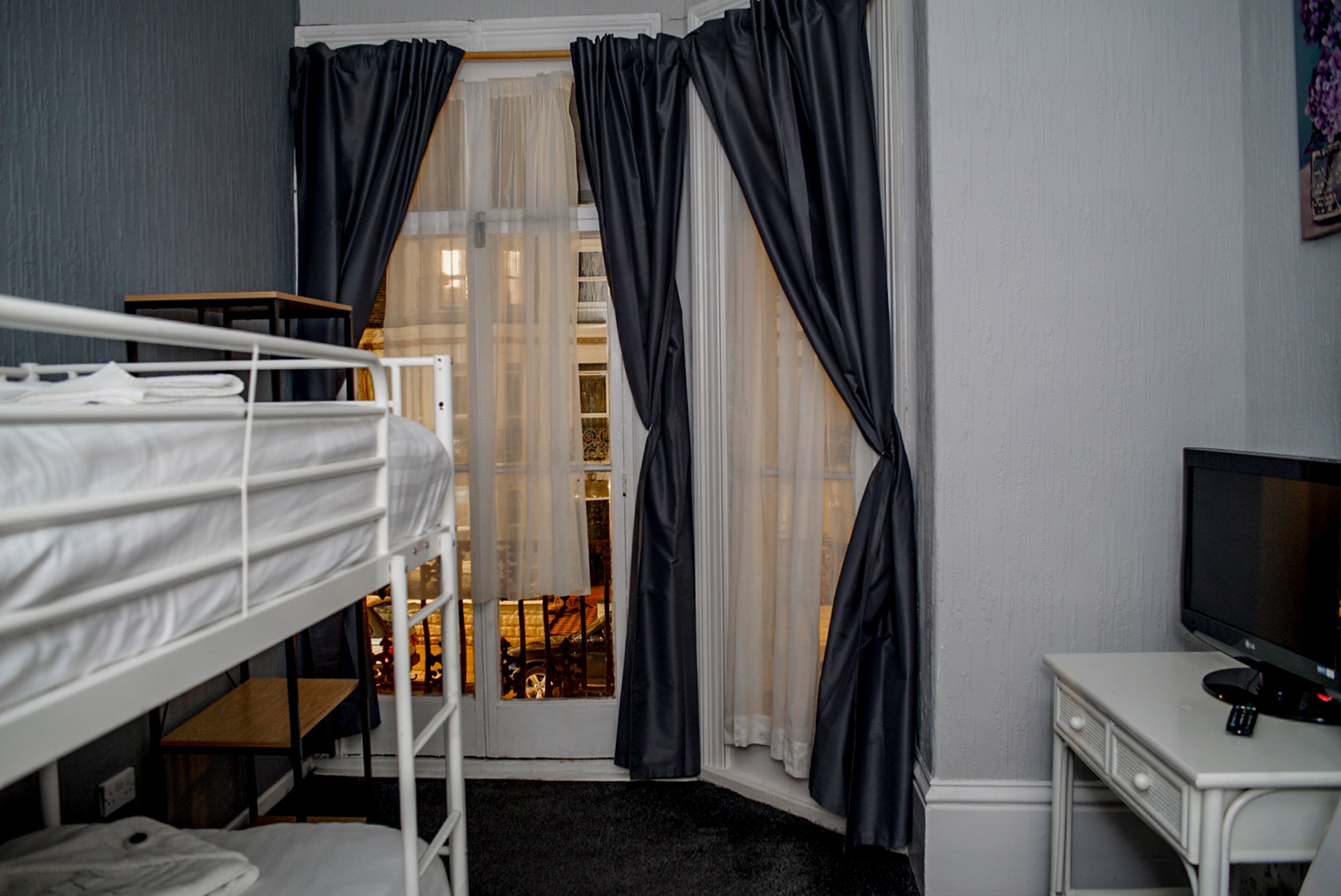 A room with a bunk bed, a desk with a computer, and a window with curtains.