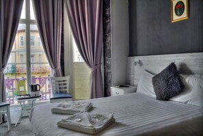 A hotel room with a bed, a chair, a small table with a kettle, and a window with curtains. - Villa Rose (Great Yarmouth)