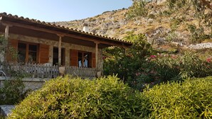 A stone building with a wooden porch and a view of a rocky hillside. - Shipwreck House (Zakynthos)