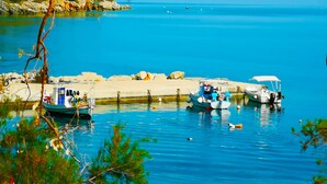 A coastal scene with boats docked at a pier, surrounded by clear blue water and rocky terrain. - Shipwreck House (Zakynthos)