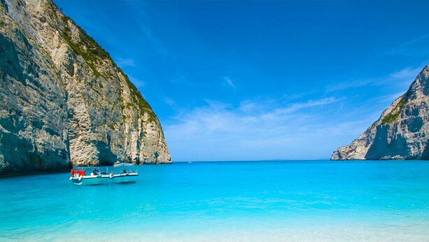 A boat on a clear turquoise sea with rocky cliffs on either side. - Shipwreck House (Zakynthos)