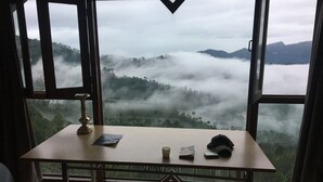 A room with a table, a chair, and a view of a misty landscape through large windows. - Dunn Perk Manor (Solan)