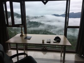 A room with a table, a chair, and a view of a misty landscape through large windows.
