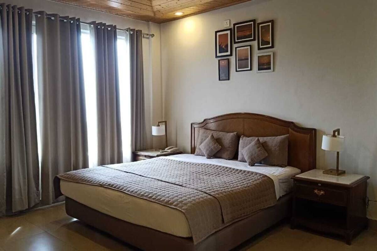 A bedroom with a large bed, a nightstand, a lamp, and a wall-mounted telephone.