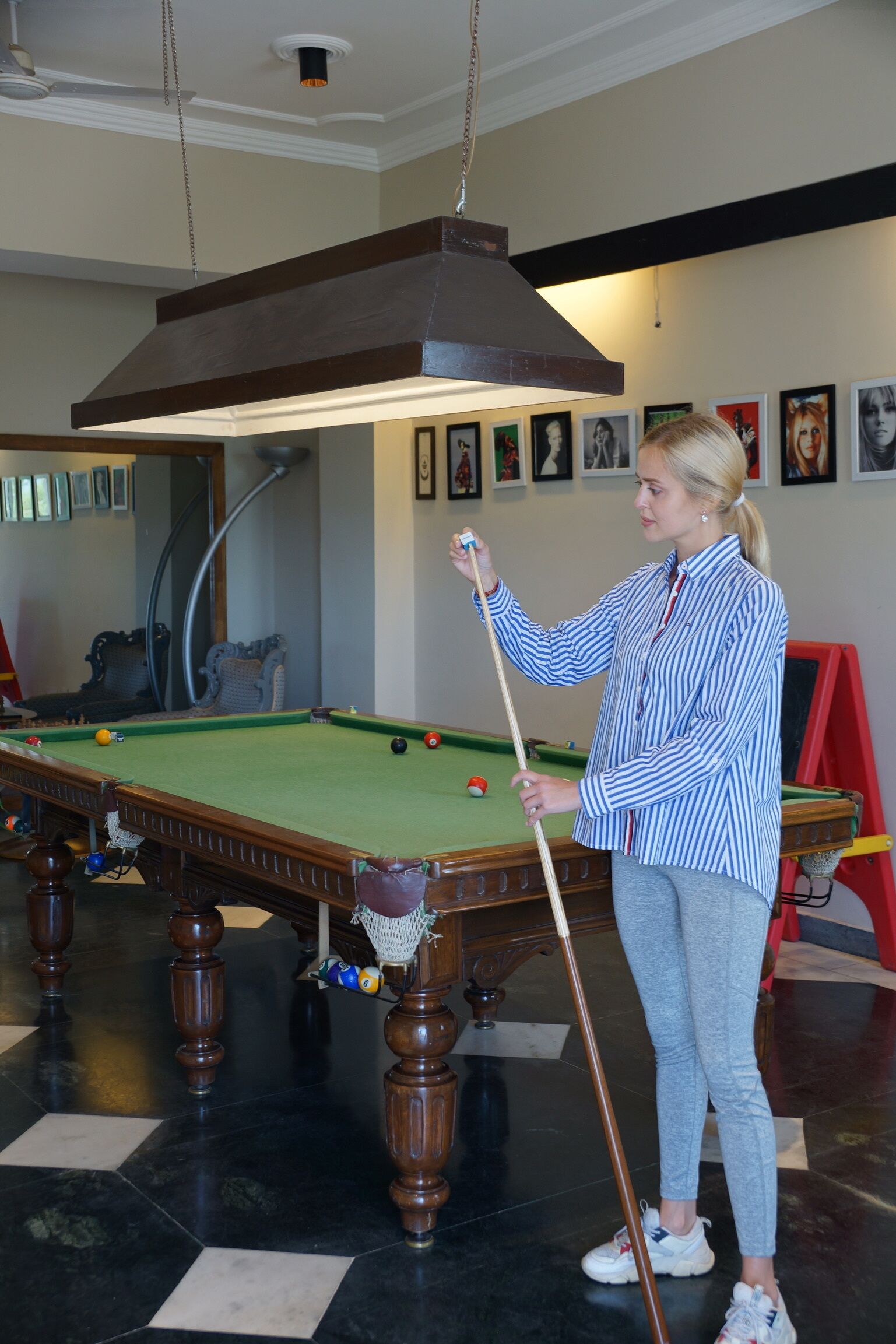 Una persona jugando billar en una habitación con una mesa de billar verde, muebles de madera y cuadros en la pared.