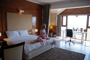 A bedroom with a large bed, a desk, and a view of the sea.