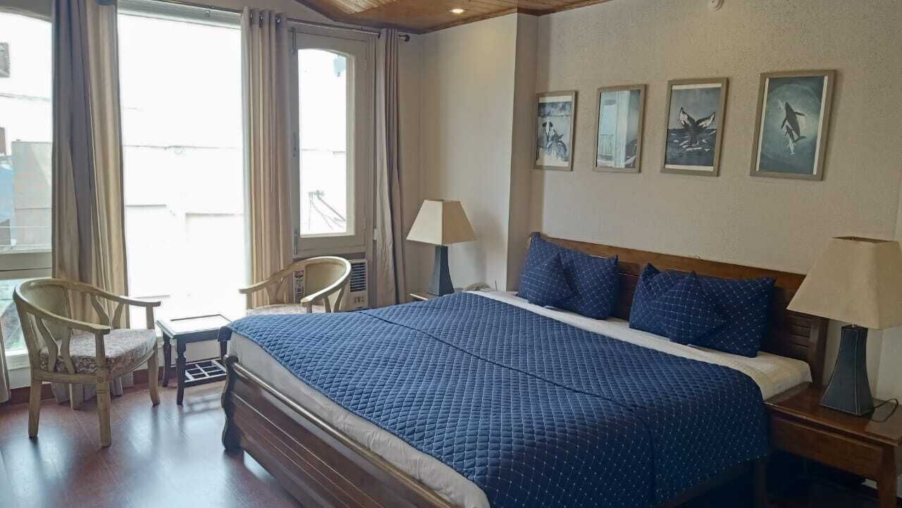 Ein Hotelzimmer mit einem großen Bett, zwei Stühlen, einem Schreibtisch und einem Fenster mit Vorhängen.