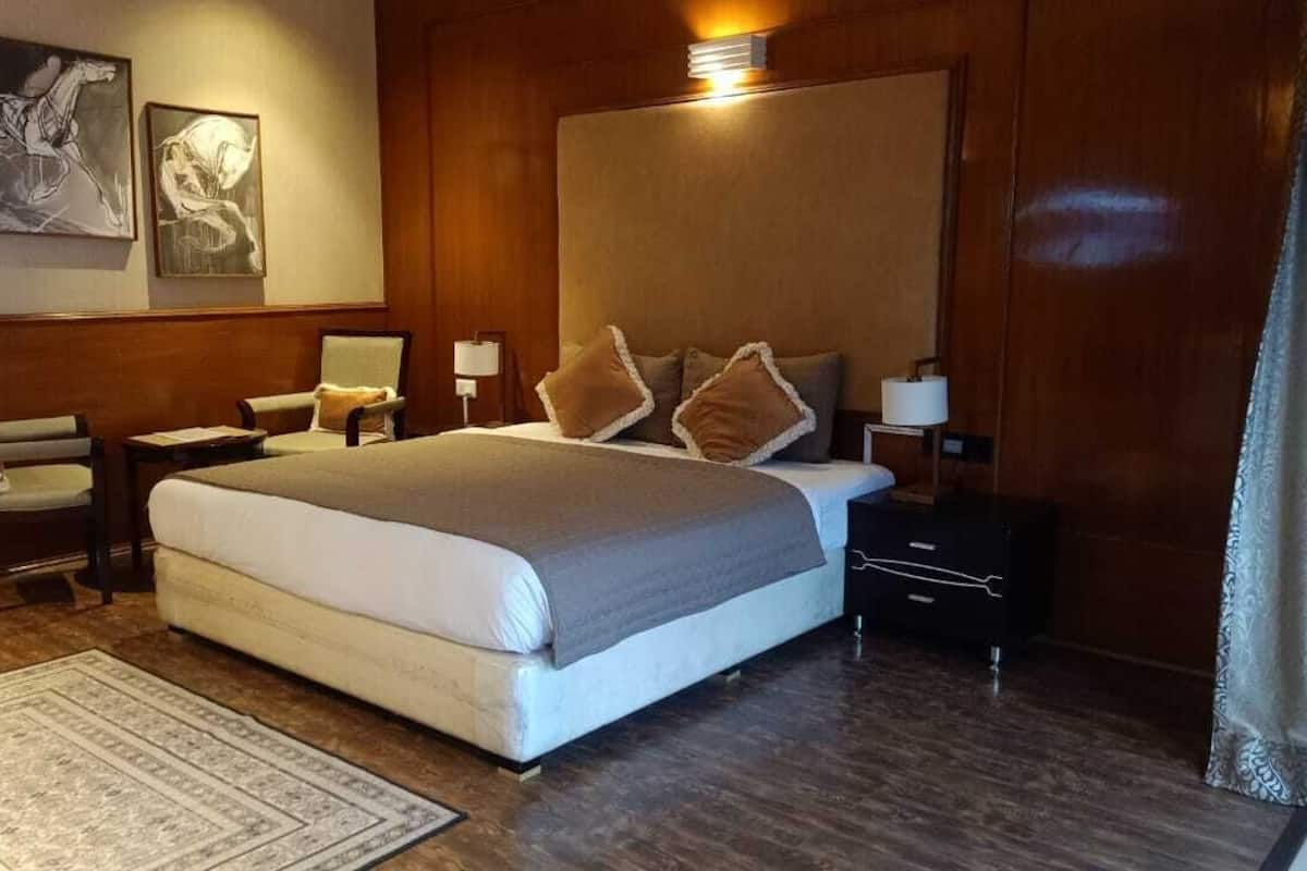 A hotel room with a large bed, wooden paneling, two bedside tables with lamps, a chair, and artwork on the wall.
