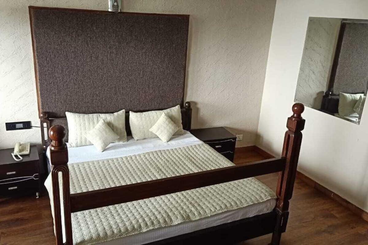 A neatly made bed with a headboard, a bedside table with a phone, and a mirror on the wall.