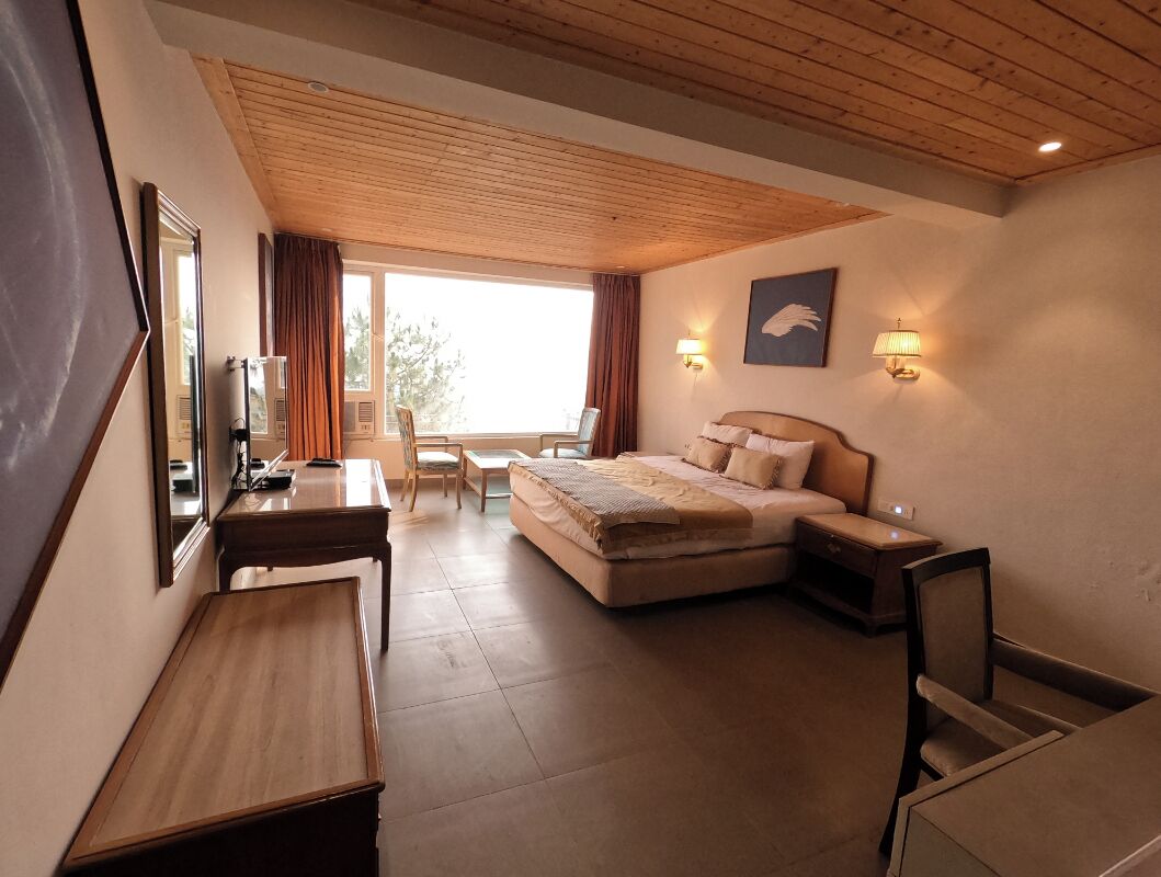 A bedroom with a bed, bedside tables, a desk, a chair, a window with curtains, and a painting on the wall.