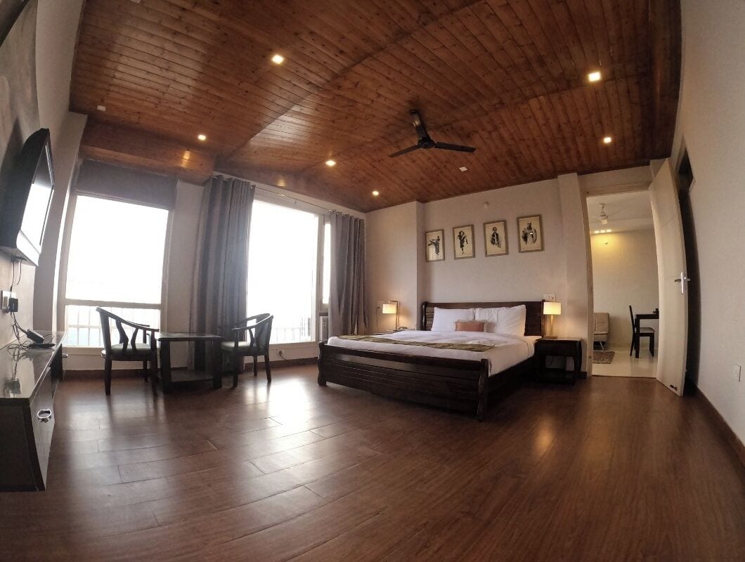 A spacious bedroom with a large bed, wooden ceiling, and a dining area with chairs.