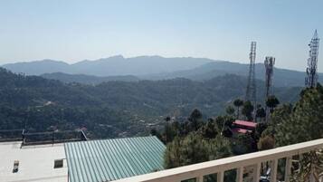 A view of a mountainous landscape with a building in the foreground featuring a green roof and a balcony.