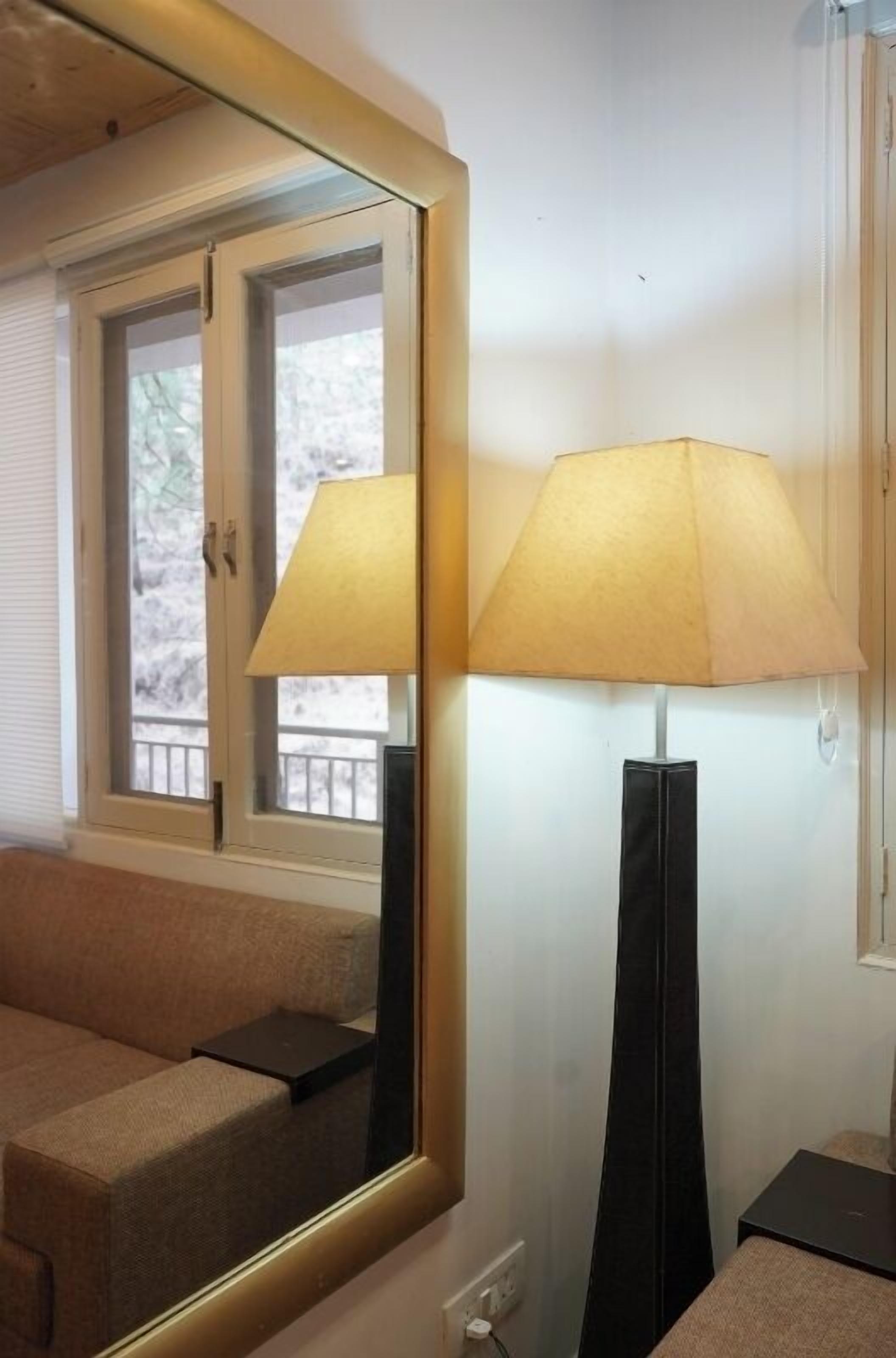A room with a large mirror reflecting a window, a lamp, and a sofa.