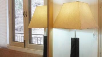 A room with a large mirror reflecting a window, a lamp, and a sofa.