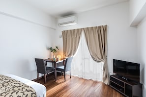 Habitación de hotel con cama, escritorio con dos sillas, televisor y equipo de aire acondicionado.