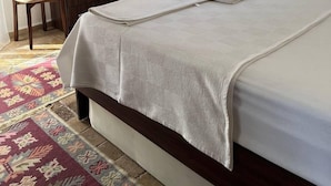 Un lit bien fait, avec une couette blanche et des oreillers, une commode en bois, une chaise, un miroir et un appareil de climatisation.