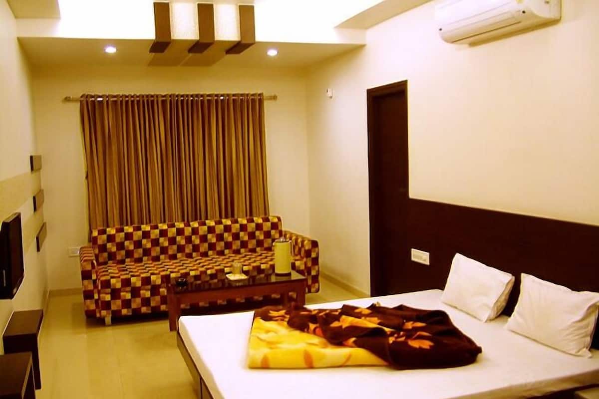 Een hotelkamer met een bed, een geruit bankje, een televisie en een airconditioner.