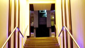 Una escalera con barandillas metálicas y suelo oscuro, que conduce a una plataforma con una lámpara.