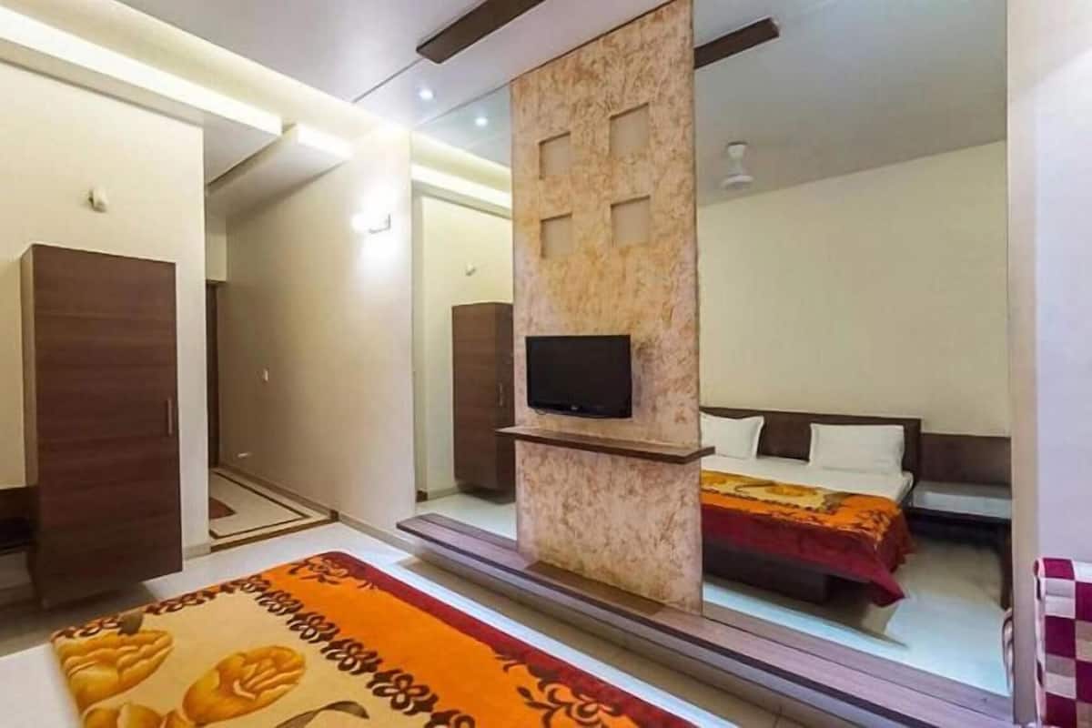 Hotelkamer met een grote spiegel, een aan een houten paneel bevestigde televisie, een bed met een rode deken en een vloerkleed met een patroon.