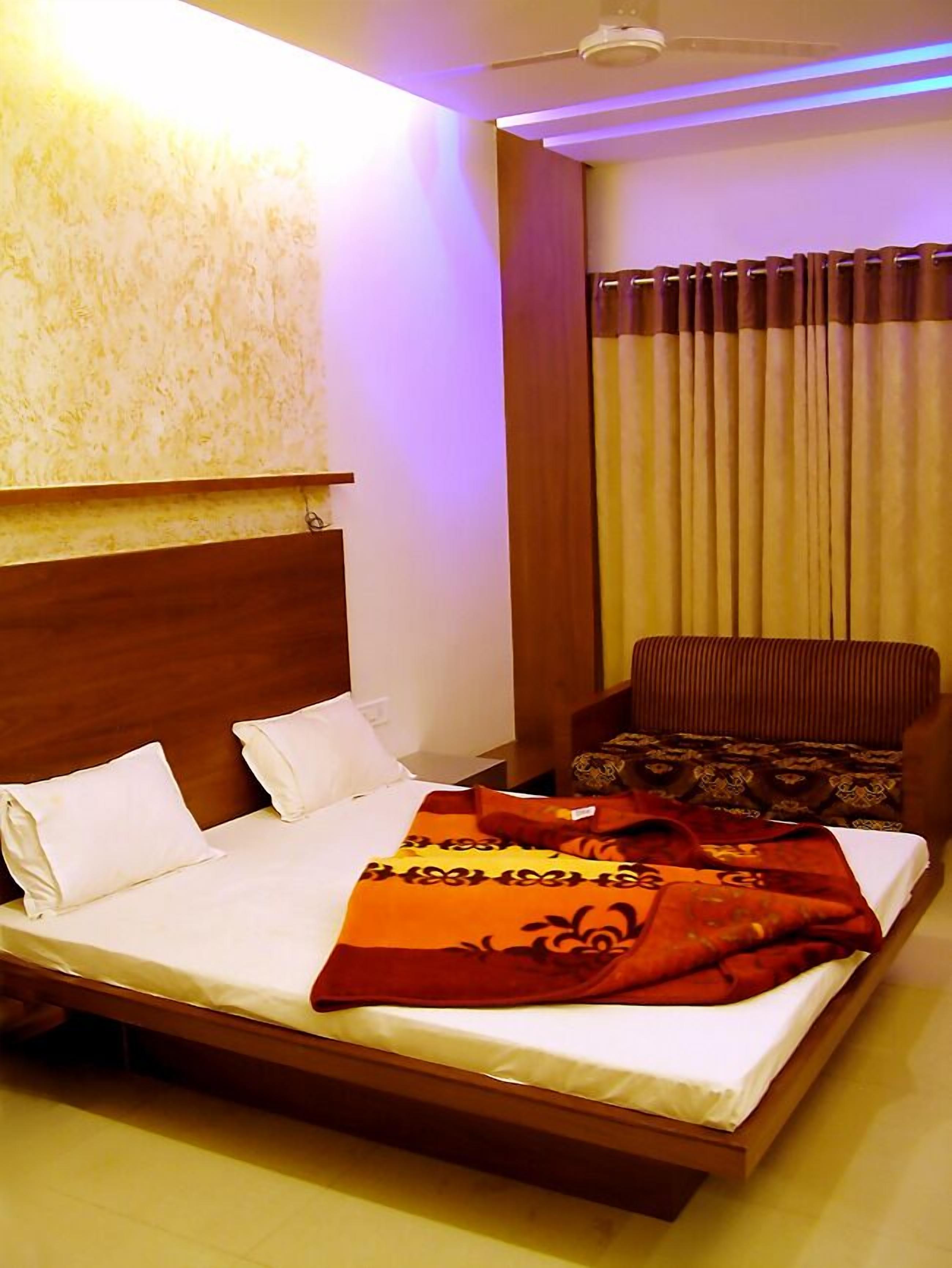 Habitación de hotel con una cama grande, cabecera de madera, una silla y una ventana con cortinas.