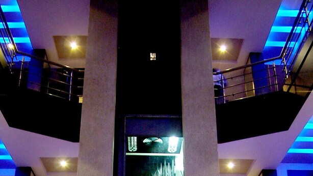 Interior de varios niveles con una escalera central, barandillas y una pantalla digital.