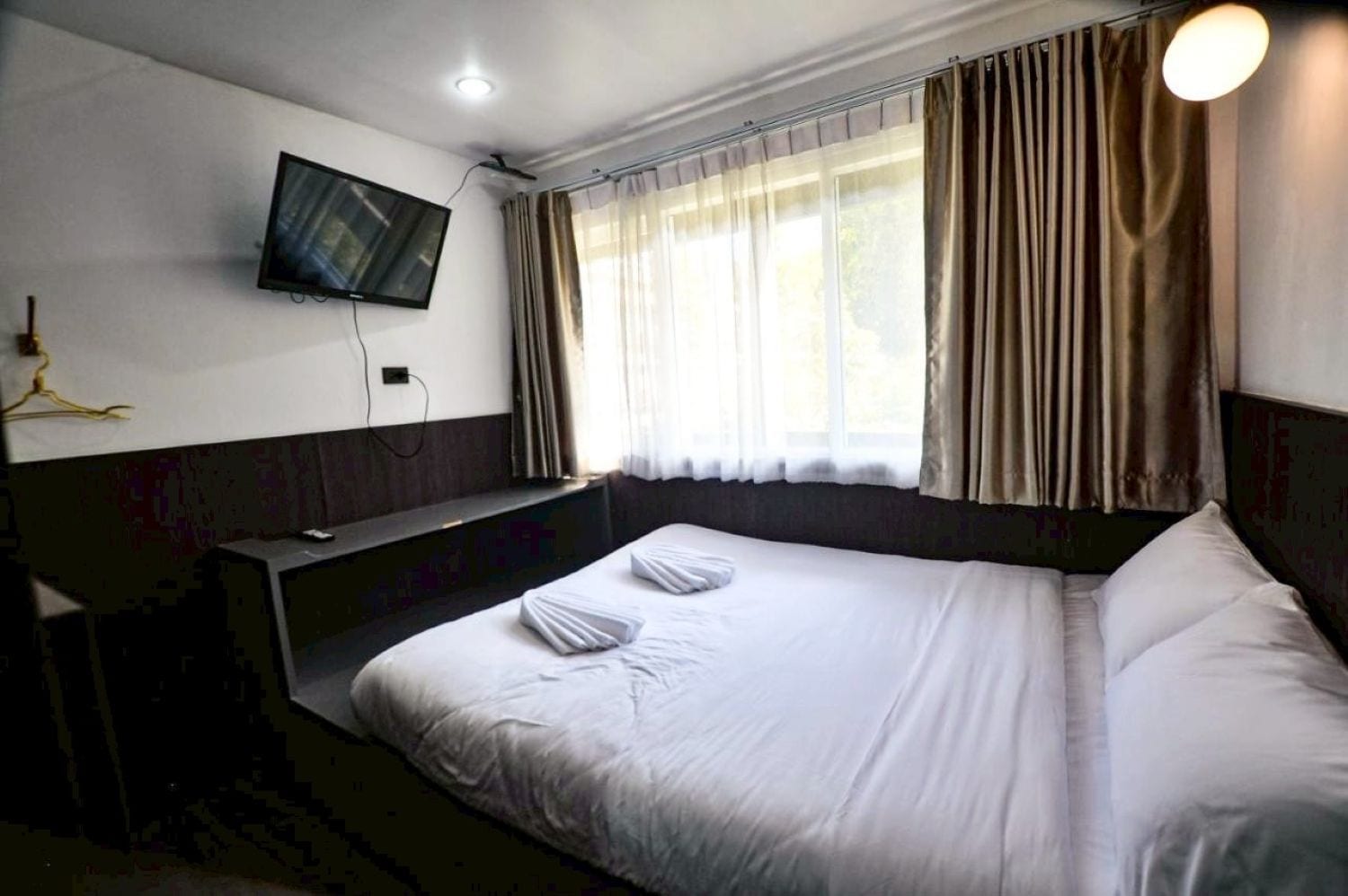A hotel room with a bed, a television mounted on the wall, and a window with curtains.