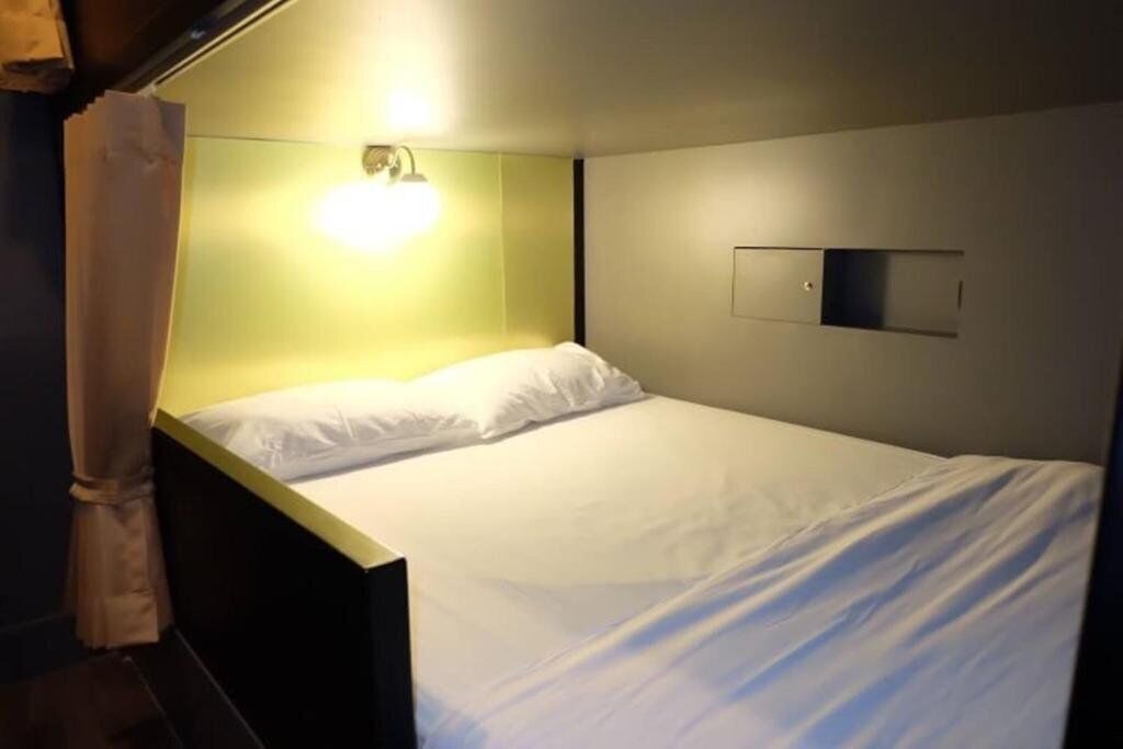 A single bed with white bedding in a room with a green accent wall and a wall-mounted light fixture.