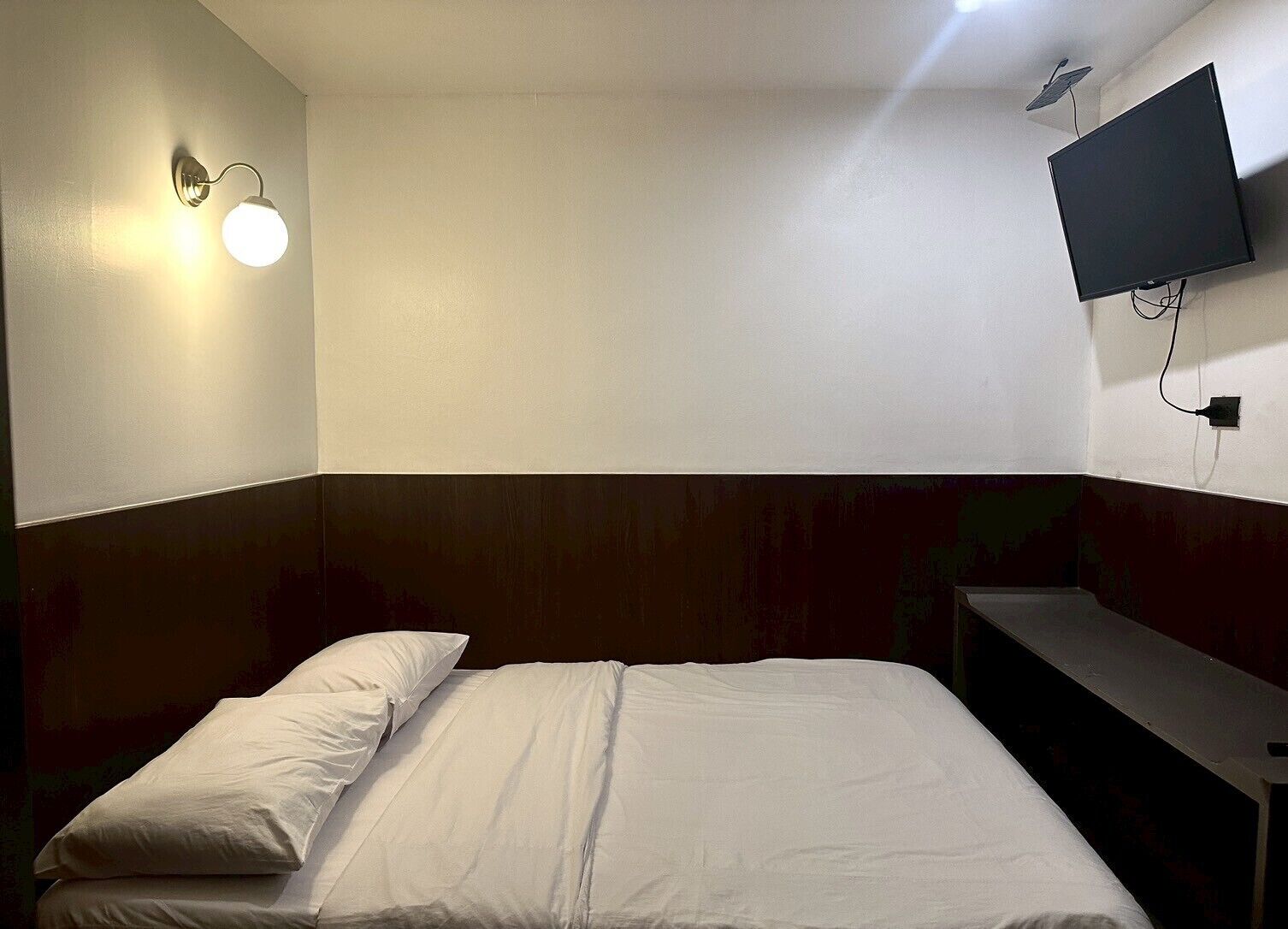 Een eenvoudige, schone kamer met een bed, een wandtelevisie en een nachtkastje.