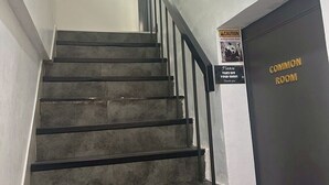 Μια σκάλα με μαύρο κάγκελο, ένα κόκκινο διακοσμητικό στοιχείο που κρέμεται και μια πινακίδα που υποδεικνύει έναν κοινόχρηστο χώρο.