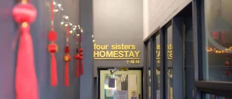 Entrada de un hotel con un cartel que dice "four sisters HOMESTAY" y caracteres chinos.